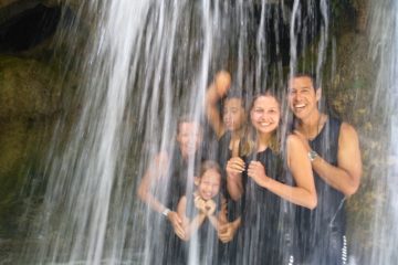 Happy family laughing as they walk through an isolated waterfall we have found on our guided tours.