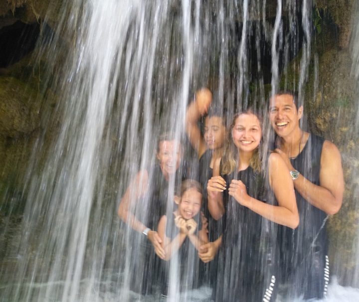 Happy family laughing as they walk through an isolated waterfall we have found on our guided tours.