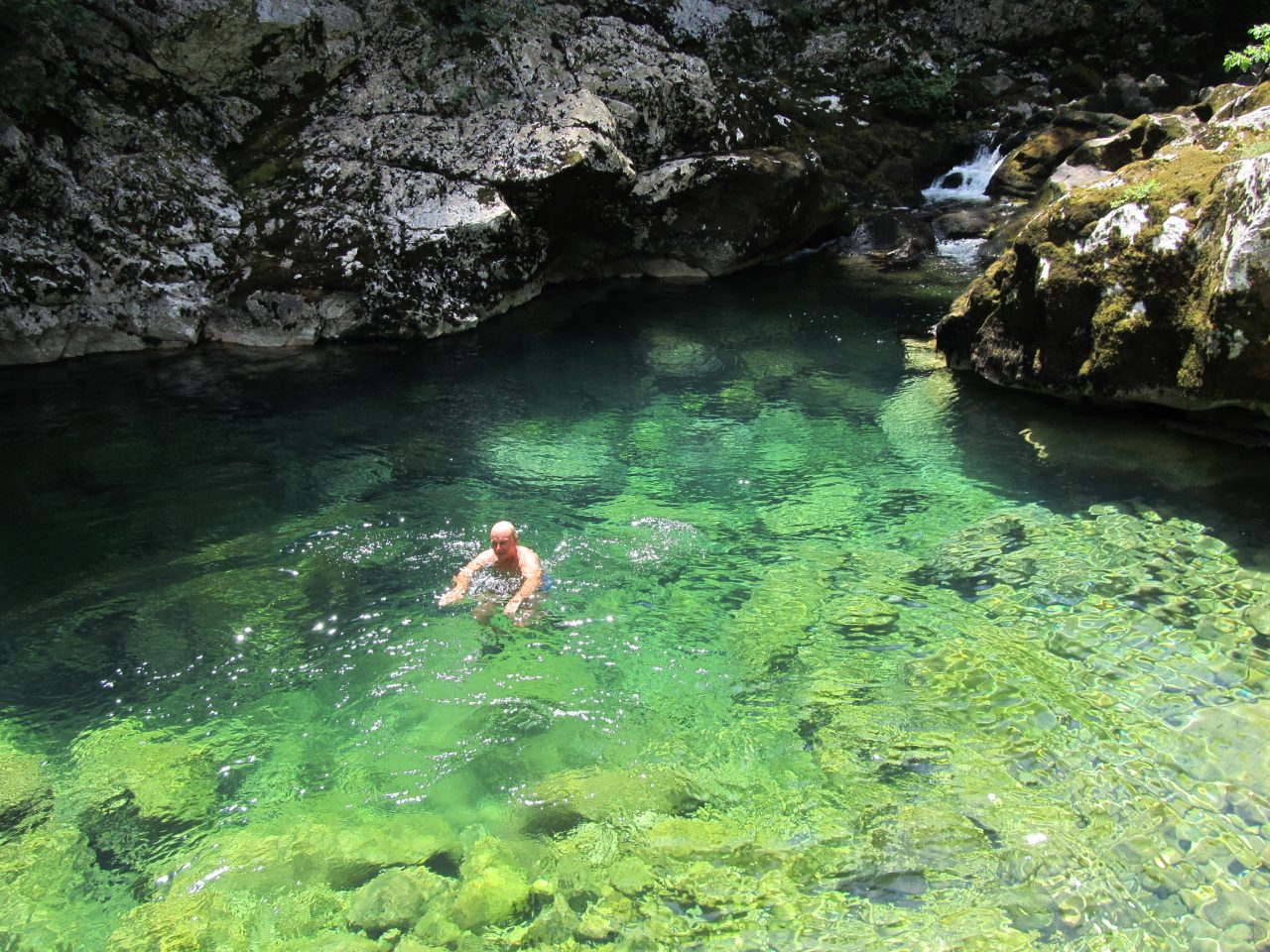 Mann auf einem Aktivitätsurlaub, der in einem kristallklaren, hellblauen Felsenbecken nahe See Skadar schwimmt