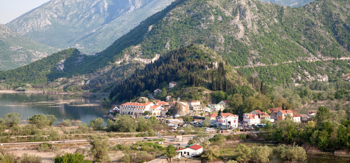 A summer view over the tiny town of Virpazar in Montenegro, next to Lake Skadar's waters, and with dried out floodplains around it and mountains above.